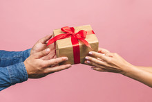 Top View Of Male And Female Hands Holding Red Gift Box With Golden Ribbon On Pink Background Flat Lay. Present For Birthday, Valentine Day, Christmas, New Year. Congratulations Background Copy Space.
