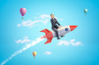 © gearstd - Young businessman riding toy rocket in blue sky with hot air balloons in background.