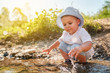 © Miljan Živković - Portrait of playful small little boy child playing with rocks and water by the lake or river in sunny day wearing hat in nature