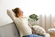 © Evrymmnt - Young beautiful woman wearing white sweater on grey textile sofa at home. Attractive slim female in domestic situation, resting on couch in her lofty apartment. Background, copy space, close up.