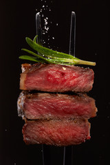 Steak concept. Closeup beef steak cuts piece slice medium well rare with rosemary and falling salt on a fork with rosemary isolated on black background.