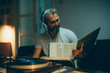 © cherryandbees - mid aged man playing records on gramophone at his home. night scene