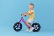 © oes - Little child boy learns to keep balance while riding a bicycle. Stylish child in yellow T-shirt on blue background