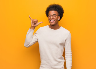 Wall Mural - Young african american man over an orange wall doing a rock gesture