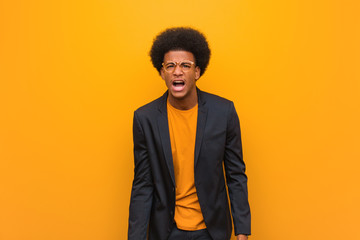 Wall Mural - Young business african american man over an orange wall screaming very angry and aggressive