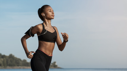 Side view shot of young woman in sportswear jogging on beach