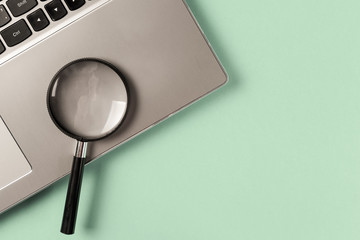 Concept information search. Laptop computer with magnifying glass on mint background. Searching information data on internet. Top view. Flat lay. Neo mint color