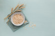 Bowl of dry oat flakes with ears of wheat on light blue background. Cooking oats porridge concept
