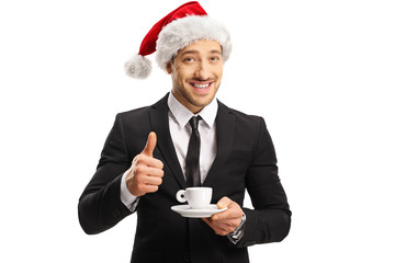 Sticker - Businessman with a Santa Claus hat holding a cup of espresso coffee and showing thumbs up