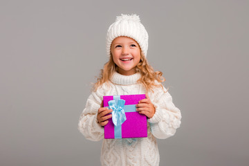 Wall Mural - little blonde girl in winter white winter hat smiling holding a pink gift box