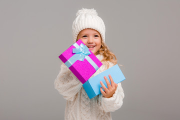 Wall Mural - little blonde girl in winter white winter hat smiling holding a pink gift box