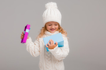 Wall Mural - little blonde girl in winter white winter hat smiling holding a pink gift box