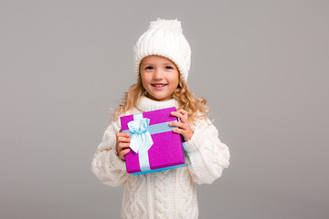 Wall Mural - little blonde girl in winter white winter hat smiling holding a pink gift box