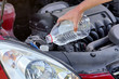 Man pouring distilled water ecological alternative to washing fluid to washer tank in car, detail on hand holding clear plastic bottle