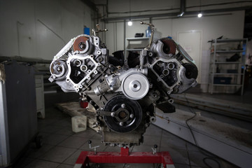 Used v8 engine mounted on a crane for installation on a car after a breakdown and renew in a vehicle repair workshop as a guarantee for the dealership. Auto service industry.