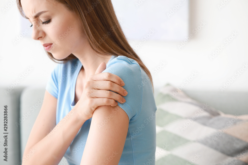 Young woman suffering from pain in shoulder at home