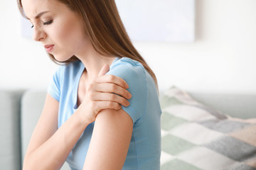 Wall Mural - Young woman suffering from pain in shoulder at home