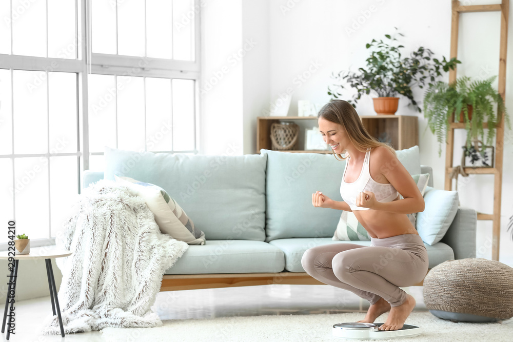 Happy young woman on scales at home. Weight loss concept