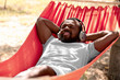 © Pixel-Shot - African-American man listening to music while relaxing in hammock outdoors