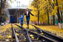 Mom And Son Walk On The Rails Of The Railway, In The Autumn Park, Near The Station, Holding Hands