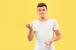 © master1305 - Caucasian young man's half-length portrait on yellow studio background. Beautiful male model in shirt. Concept of human emotions, facial expression, sales, ad. Pointing and showing something.