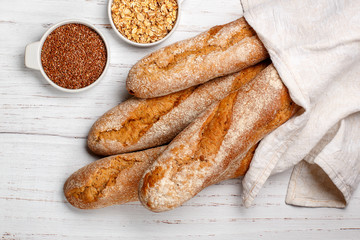 Wall Mural - Freshly baked homemade cereal baguettes with oatmeal and flax seed on a white wooden table. Selective focus.