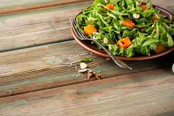 Wall Mural - Paleo diet salad with arugula, baked pumpkin, hazelnut and sesame seeds on brown plate. Healthy food concept with copy space.