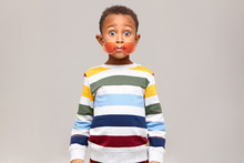 Oops. Funny Bug Eyed Dark Skinned Little Boy In Stylish Multicolored Jumper Staring At Camera In Full Disbelief, Round Pink Sunglasses Slipped Off His Eyes. Surprise, Shock And Astonishment