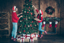Full Size Profile Side Photo Of Two Romantic Spouses People Holding Baubles Decorate Christmas Tree For X-mas Wearing Cap Hat In House Full Of Newyear Decoration Lights Illumination Indoors