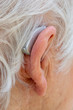 Hearing aid. Female pensioner with white hair wearing a Behind The Ear, BTE, hearing aid. Close up of ear and device viewed from behind.