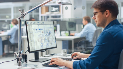 Poster - Over the Shoulder Shot of Engineer Working with CAD Software on Desktop Computer, Screen Shows Technical Drafts and Drawings. In the Background Engineering Facility Specialising on Industrial Design