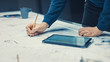 © Gorodenkoff - In the Dark Industrial Design Engineering Facility: Male Engineer Works with Blueprints Laying on a Table, Uses Pencil, Ruler and Digital Tablet. On Desktop Multiple Drawings. Focus on Hands