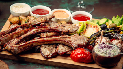 Grilled lamb ribs served on wooden plate with vegetables and four souces