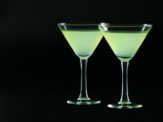 A classic daiquiri alcoholic cocktail of light green color from white rum, simple syrup and lime juice, in two conical cocktail glasses on a dark background