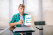 © GENETTICA - Young business man sitting at office desk looking at camera and pointing at a tablet with financial information displayed in graphical form (column graph, stacked bar graph and pie graph). Screen gra