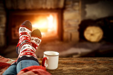 Woman Legs With Christmas Wool Socks And Fireplace 