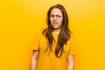 Wall Mural - young pretty woman feeling puzzled and confused, with a dumb, stunned expression looking at something unexpected against orange background