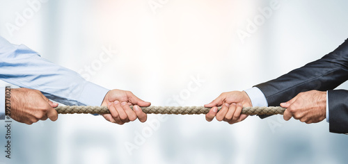 Tug of war, two businessman pulling a rope in opposite directions over defocused Tableau sur Toile