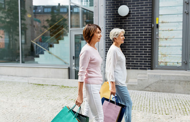 Wall Mural - sale, consumerism and people concept - two senior women or friends with shopping bags walking along tallinn city street