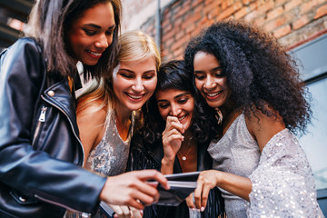 Wall Mural - Four smiling women choosing instant photographs outdoors