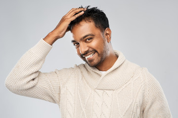 Poster - emotion, expression and people concept - smiling indian man in knitted woollen sweater touching his hair over gray background