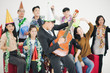 © linghaa - Group of cheerful joyful Asia young people standing and sitting celebrating together around red sofa with balloon in white background, new year party concept. man playing guitar in front of crowd.