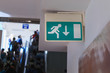 Emergency exit sign in corridor mounted on a wall. People walking in corridor background