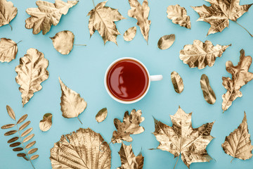 Wall Mural - top view of tea in mug near golden foliage on blue background