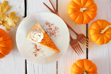 Wall Mural - Slice of pumpkin pie cheesecake with whipped cream, top view table scene on a white wood background