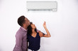 © Andrey Popov - Couple Adjusting Temperature Of Air Conditioner