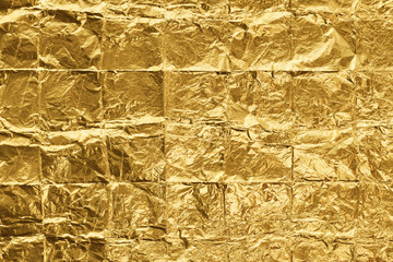 Golden color folded into squares and crumpled foil background. Wrinkled light gold metallic texture. Closeup