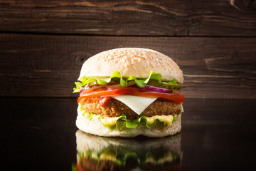 Delicious fast food. Delicious tasty burger with lettuce, cheese, onion and tomato on a rustic wooden plank on a black background