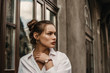 © Victoria Fox - Outdoor fashion portrait of elegant, luxury brunette woman wearing golden circle earrings, brown wrist watch, trendy white shirt, posing in street of European city. Copy, empty space for text