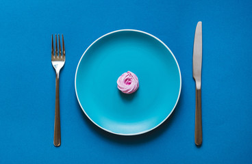 Flat lay  - Delicious and fresh pink desserts on color plate with fork and knife on blue background.